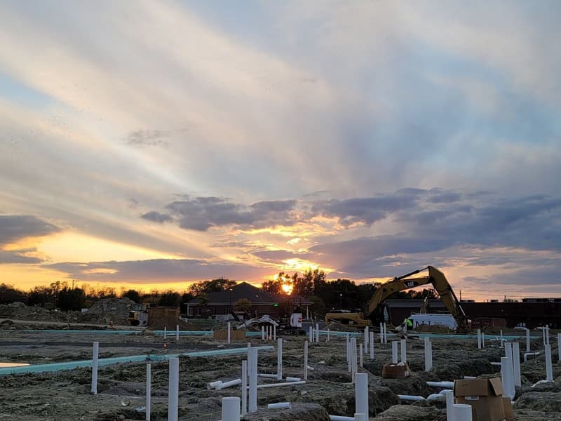 Plumbing stubs and excavator on site at sunset